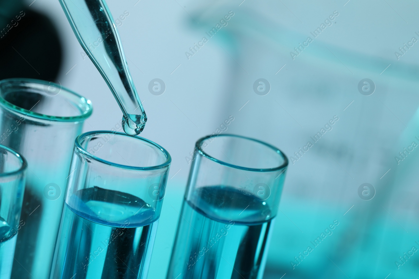 Photo of Dripping liquid from pipette into test tube on blurred background, closeup. Space for text