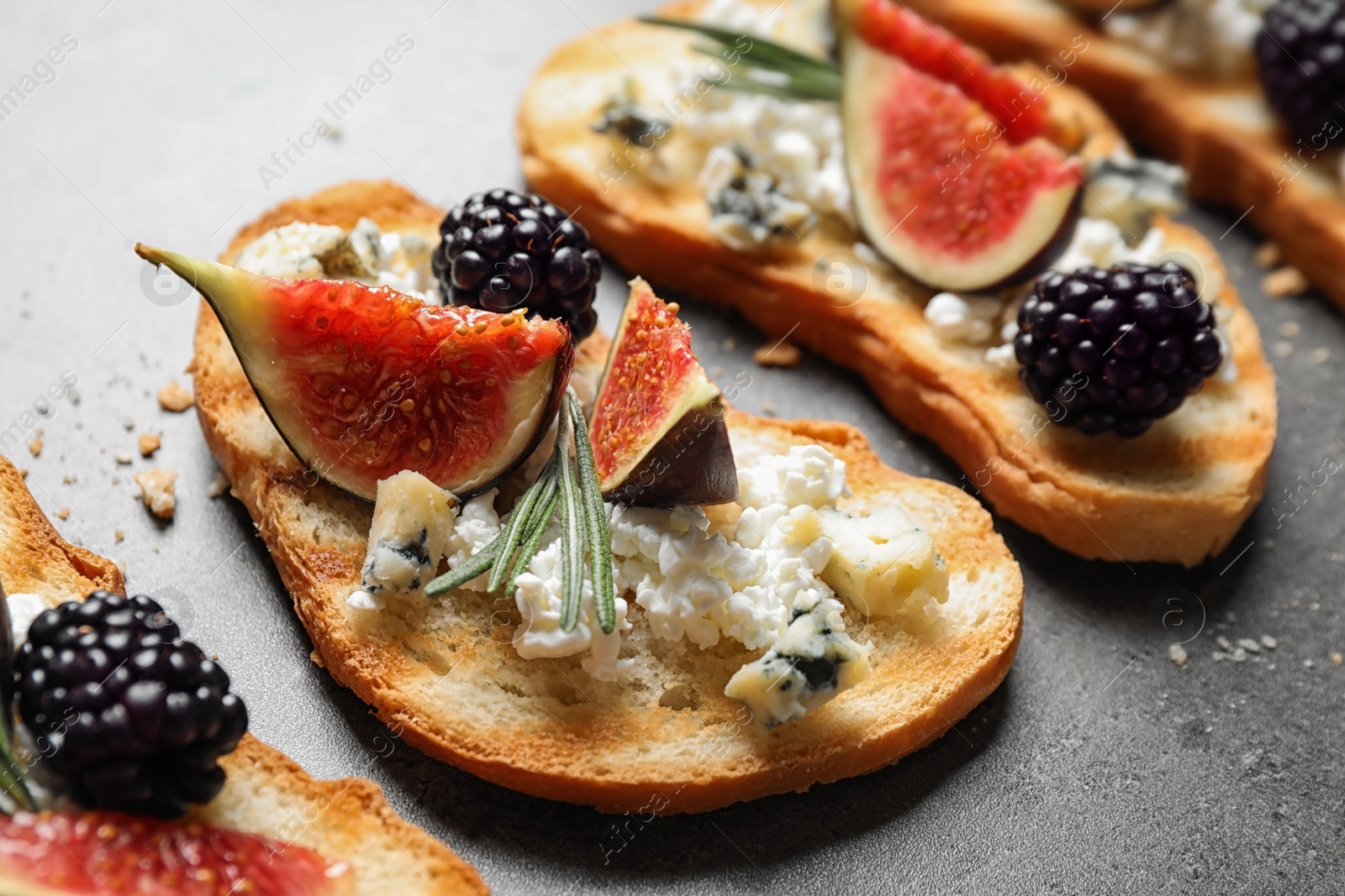 Photo of Bruschettas with cheese, figs and blackberries on grey table, closeup