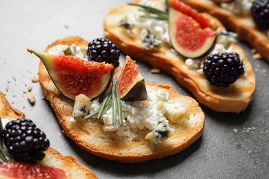 Photo of Bruschettas with cheese, figs and blackberries on grey table, closeup