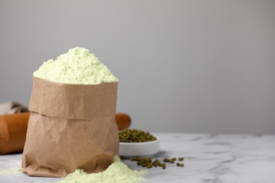 Photo of Mung bean flour in paper bag and seeds on white marble table, space for text