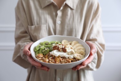 Photo of Woman holding bowl of tasty granola indoors, closeup