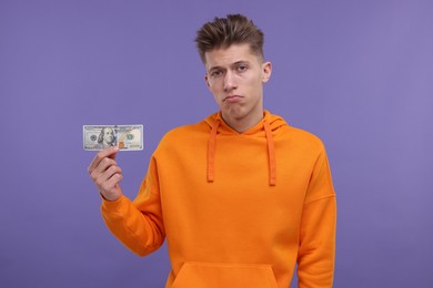 Upset man with dollar banknote on purple background