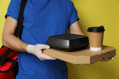 Photo of Courier in protective gloves holding order on yellow background, closeup. Food delivery service during coronavirus quarantine