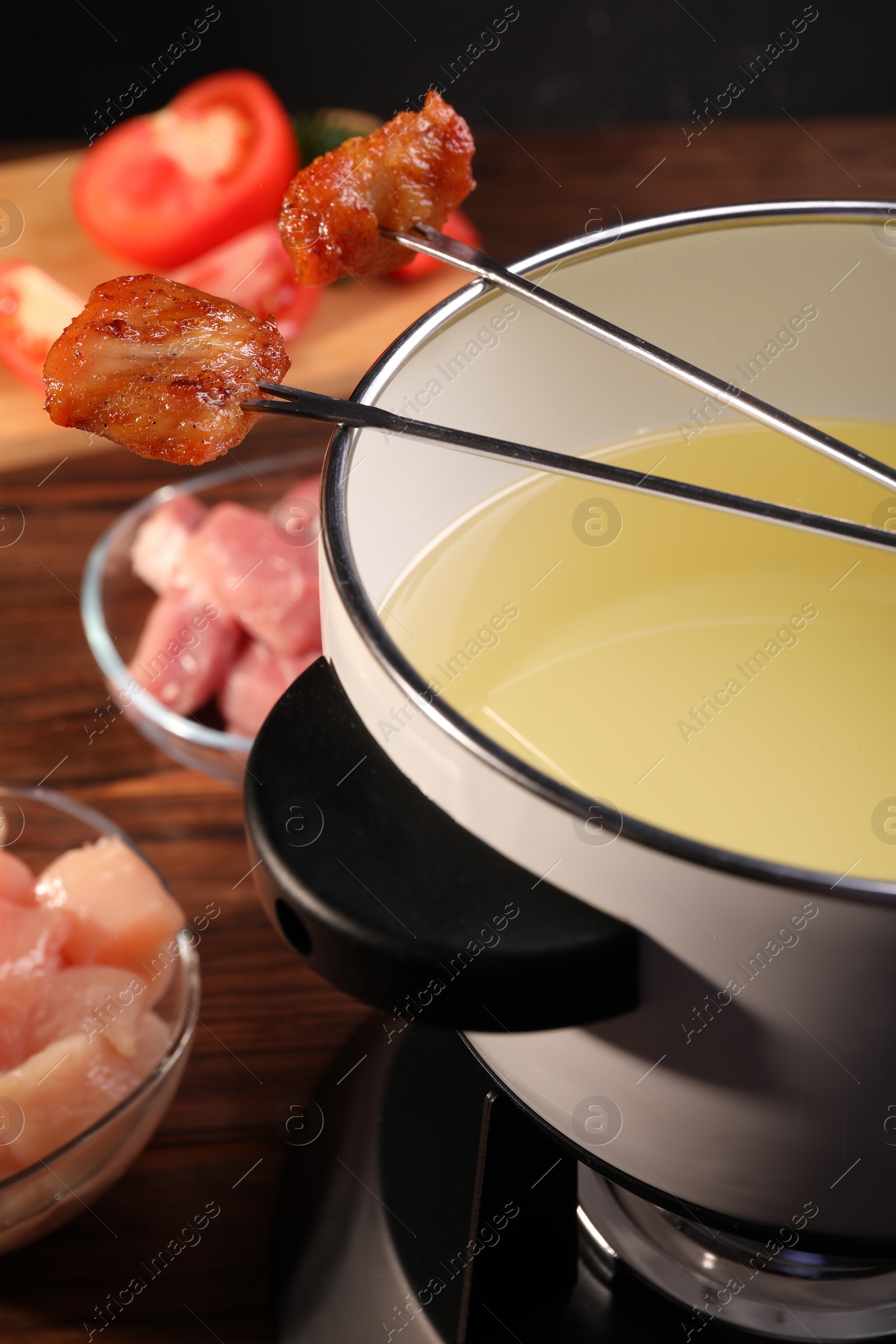 Photo of Fondue pot, forks with fried meat pieces and other products on wooden table, closeup