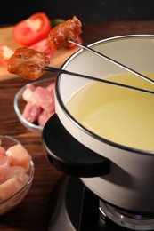 Fondue pot, forks with fried meat pieces and other products on wooden table, closeup