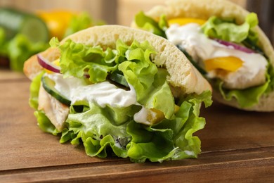 Photo of Delicious pita sandwiches with chicken breast and vegetables on wooden table, closeup