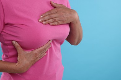 Woman doing breast self-examination on light blue background, closeup. Space for text