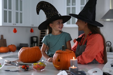 Photo of Mother and daughter making pumpkin jack o'lanterns at table in kitchen. Halloween celebration
