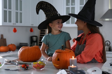 Mother and daughter making pumpkin jack o'lanterns at table in kitchen. Halloween celebration