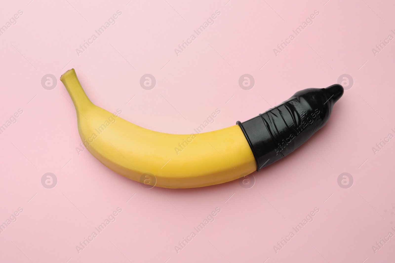 Photo of Banana with condom on pink background, top view. Safe sex concept