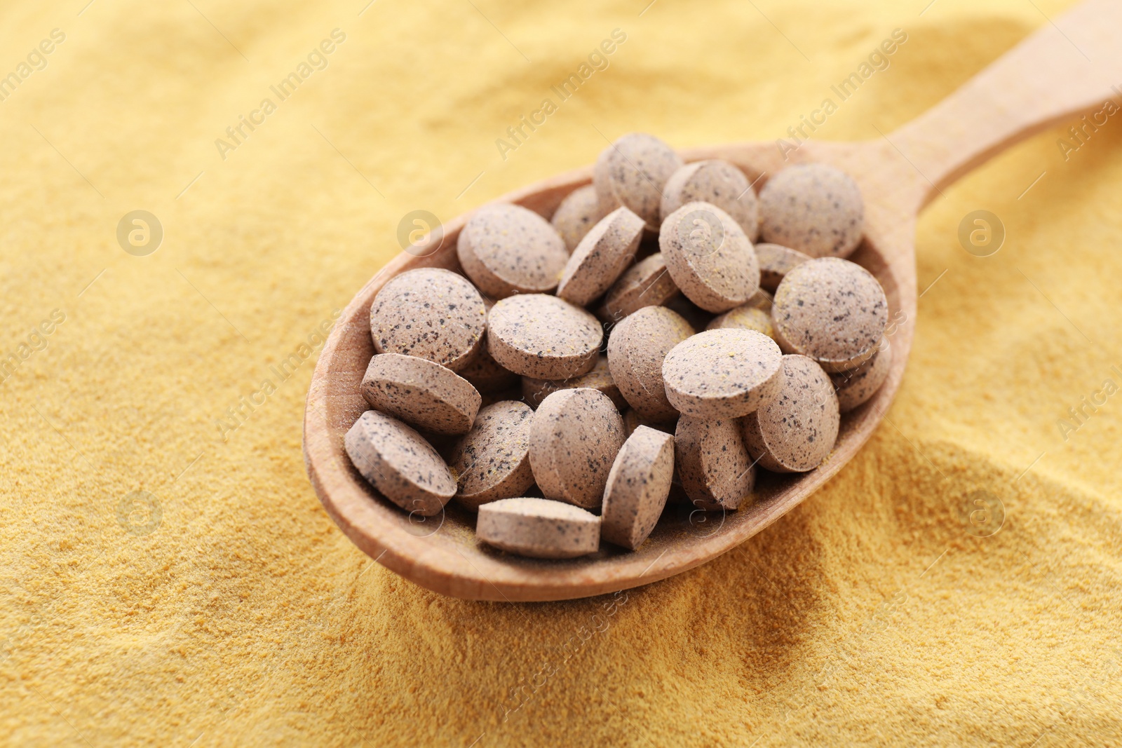 Photo of Wooden spoon of brewer`s yeast tablets on powder, closeup