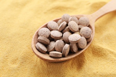 Photo of Wooden spoon of brewer`s yeast tablets on powder, closeup