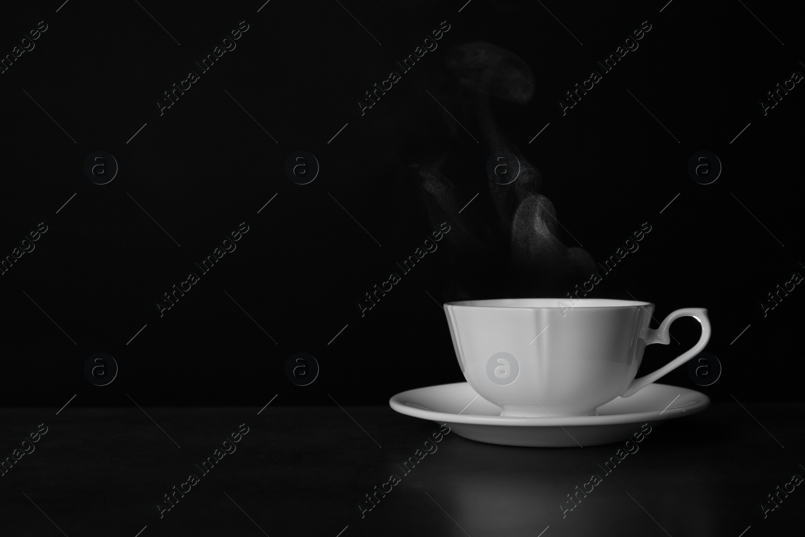 Photo of Ceramic cup of hot fresh tea on table against black background, space for text