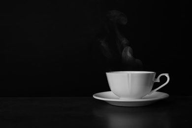 Photo of Ceramic cup of hot fresh tea on table against black background, space for text