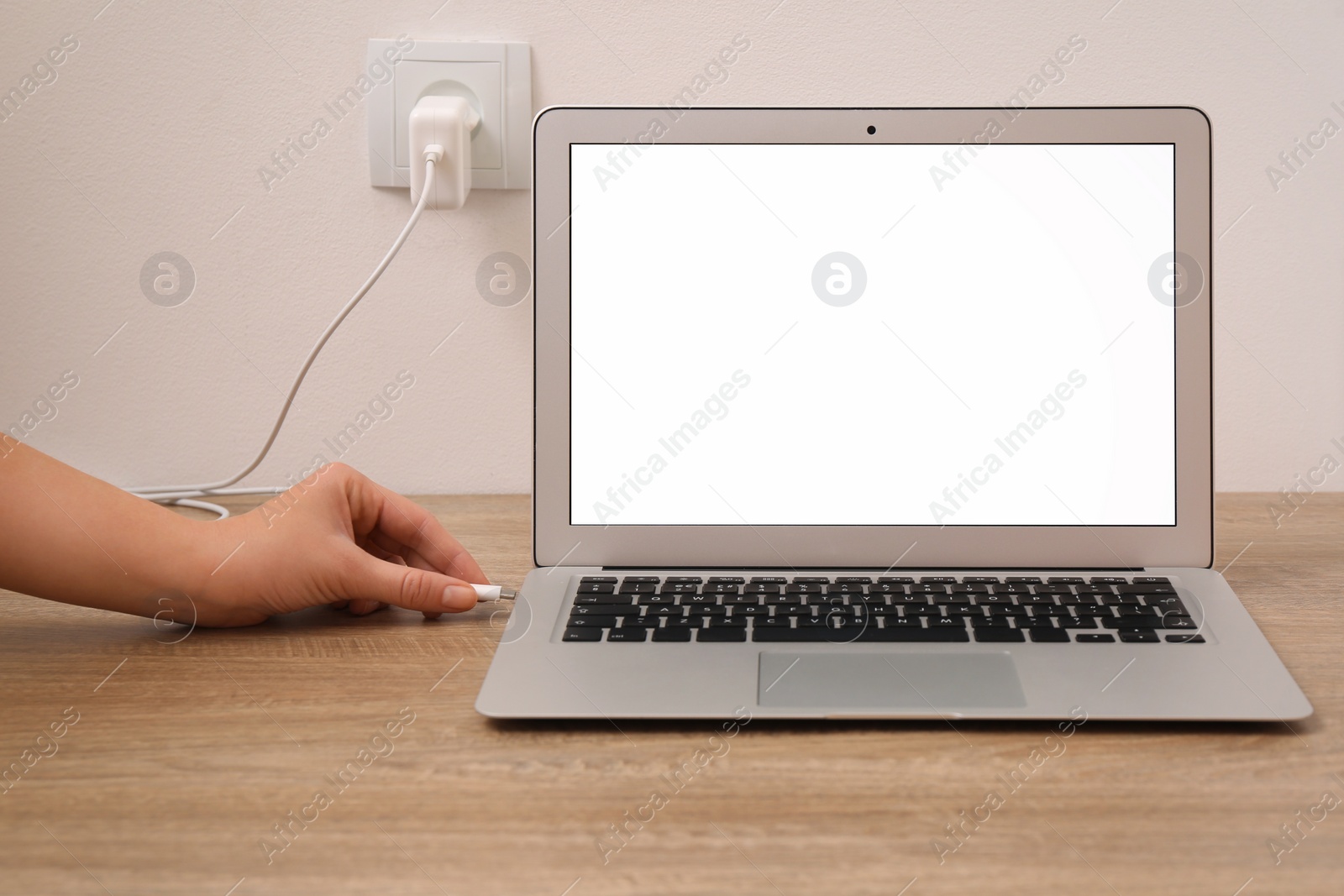 Photo of Woman connecting charge cable to laptop on wooden table, closeup. Space for text