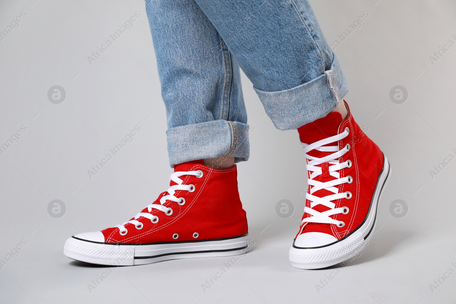 Photo of Woman wearing pair of new stylish sneakers on light grey background, closeup