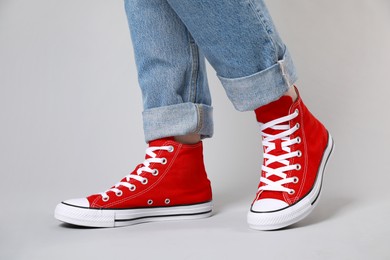 Photo of Woman wearing pair of new stylish sneakers on light grey background, closeup