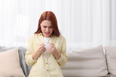 Angry woman popping bubble wrap on sofa at home, space for text. Stress relief