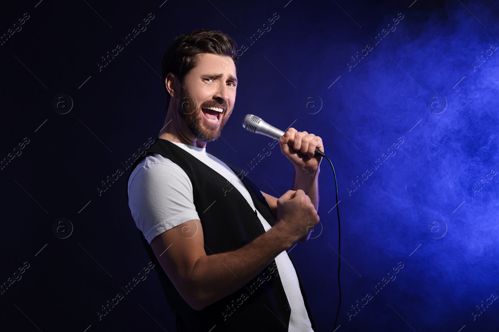 Photo of Handsome man with microphone singing on dark blue background