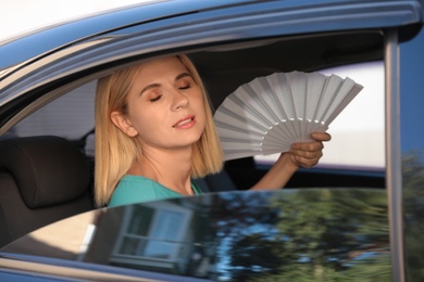 Woman with hand fan suffering from heat in car. Summer season