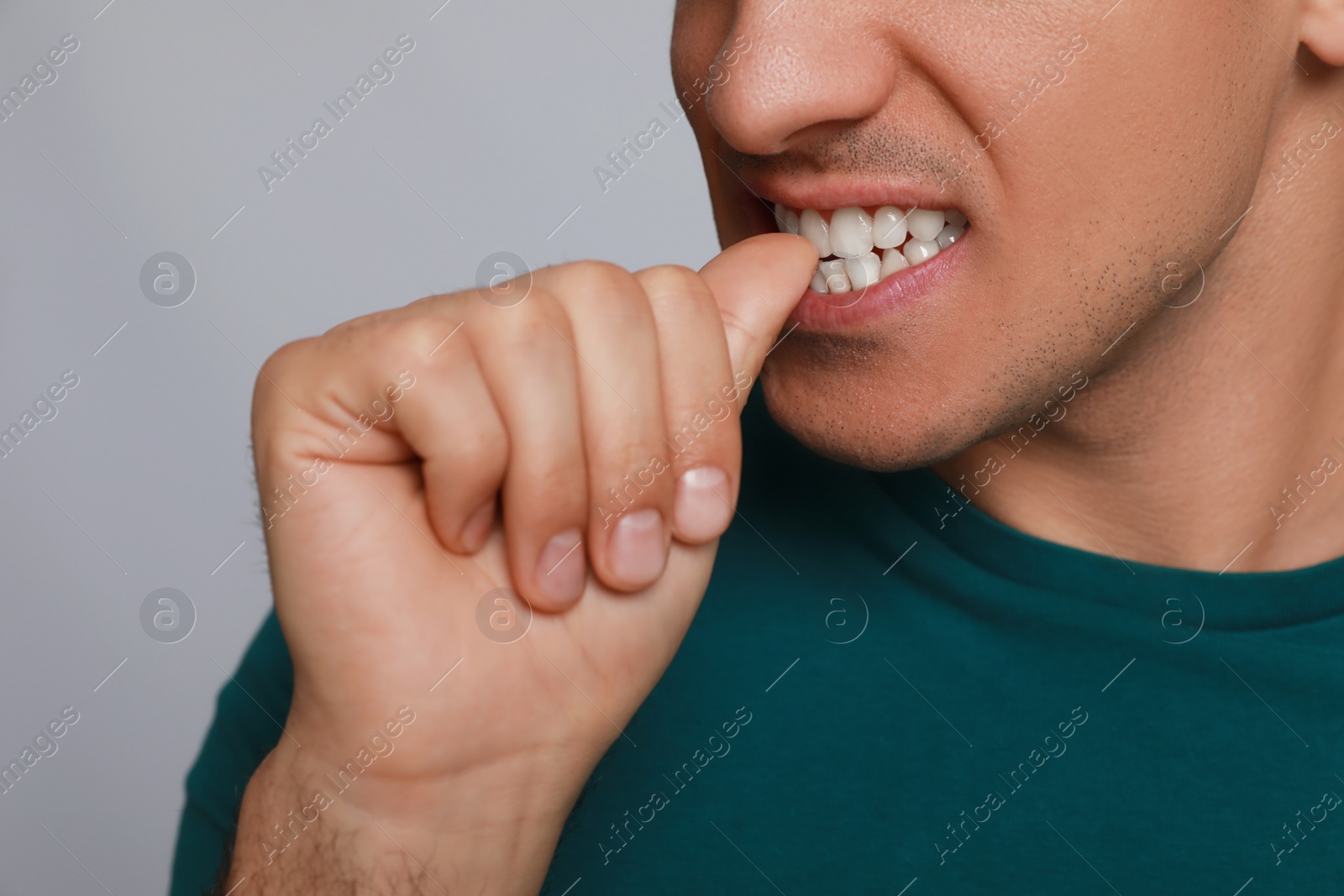 Photo of Man biting his nails on grey background, closeup. Bad habit