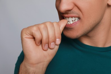 Photo of Man biting his nails on grey background, closeup. Bad habit