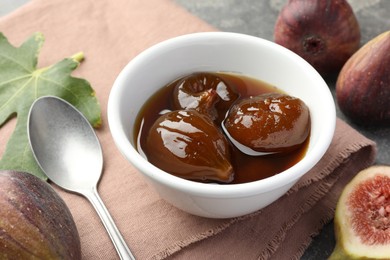 Photo of Bowl of tasty sweet jam, fresh figs and spoon on grey table, closeup