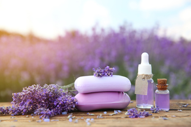 Photo of Fresh lavender flowers, soap bars and essential oil on wooden table outdoors, closeup
