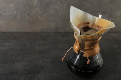 Photo of Glass chemex coffeemaker with coffee on gray table, space for text