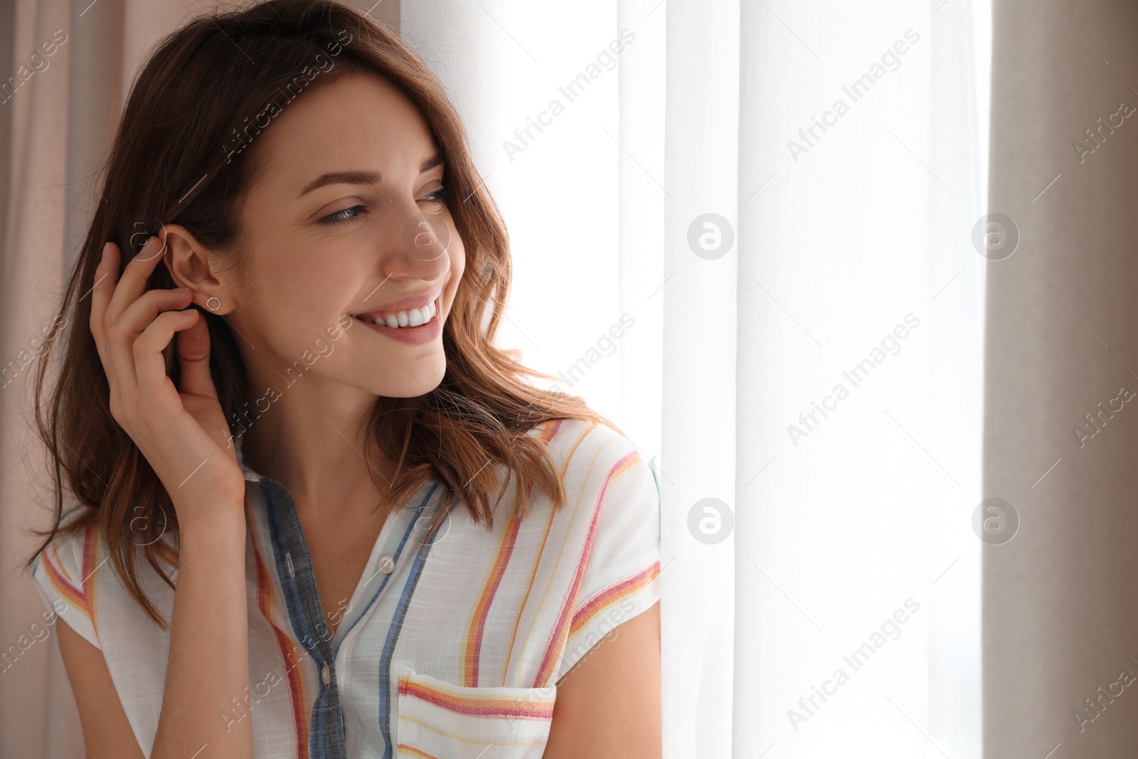 Photo of Young woman near window with beautiful curtains at home