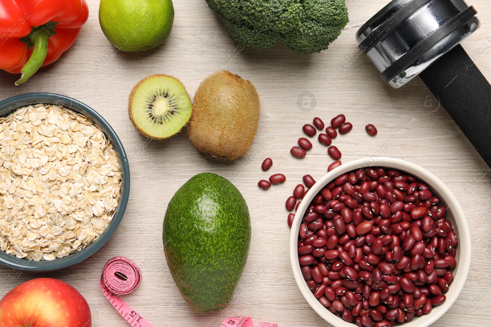 Photo of Healthy diet. Different products, dumbbell and measuring tape on light wooden table, flat lay