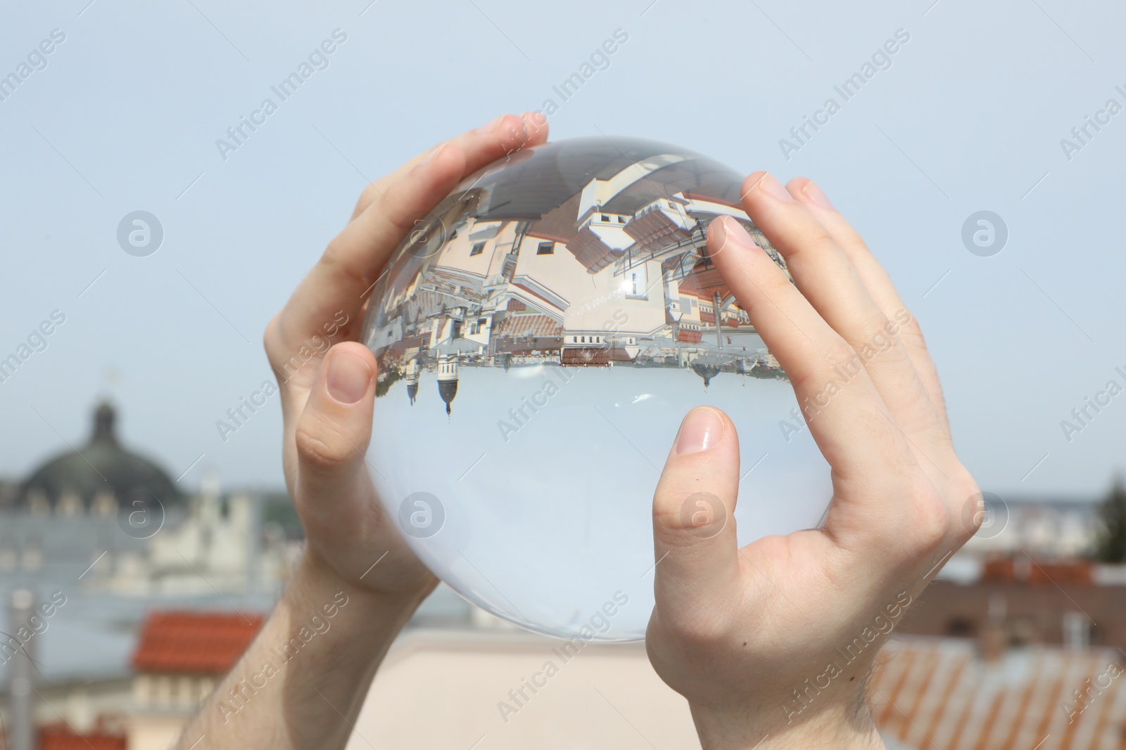 Photo of View of beautiful city street, overturned reflection. Man holding crystal ball against sky, closeup