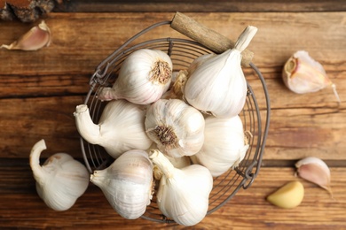 Photo of Fresh organic garlic in basket on wooden table, flat lay