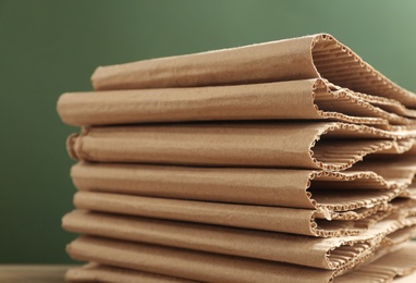 Photo of Stack of cardboard against green background, closeup. Recycling concept