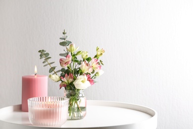 Photo of Stylish tender composition with burning candles and flowers on white table against light background, space for text. Cozy interior element