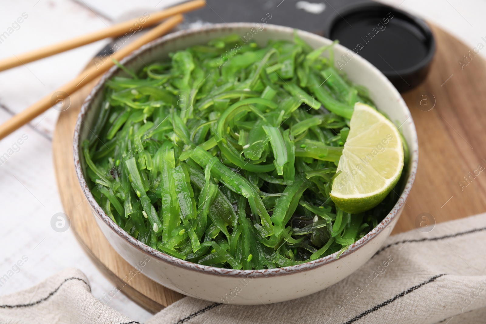 Photo of Tasty seaweed salad in bowl served on wooden table, closeup