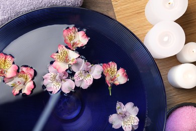 Photo of Bowl of water with flowers, candles and sea salt on table, top view. Spa treatment