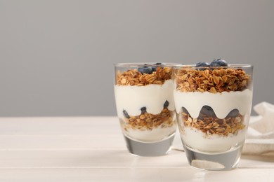 Glasses of tasty yogurt with muesli and blueberries served on white wooden table, space for text