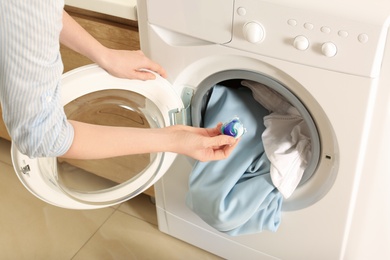 Photo of Woman putting laundry detergent capsule into washing machine indoors, closeup