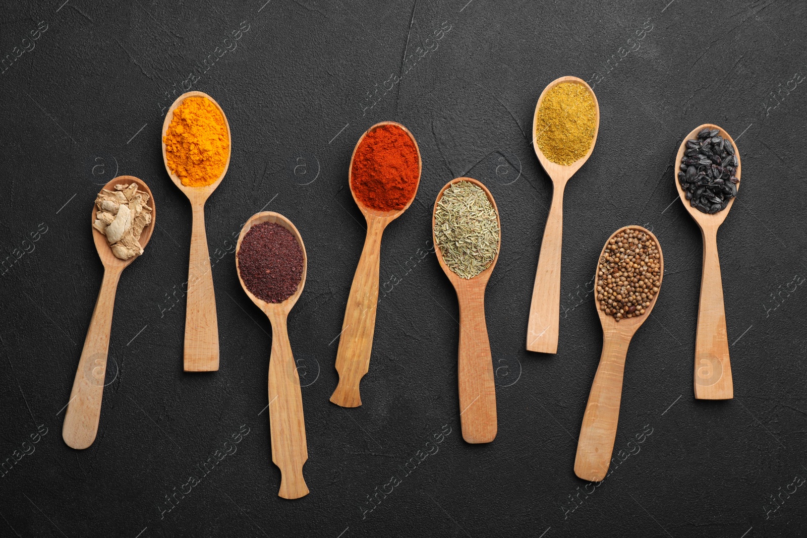 Photo of Composition with different aromatic spices in wooden spoons on dark background