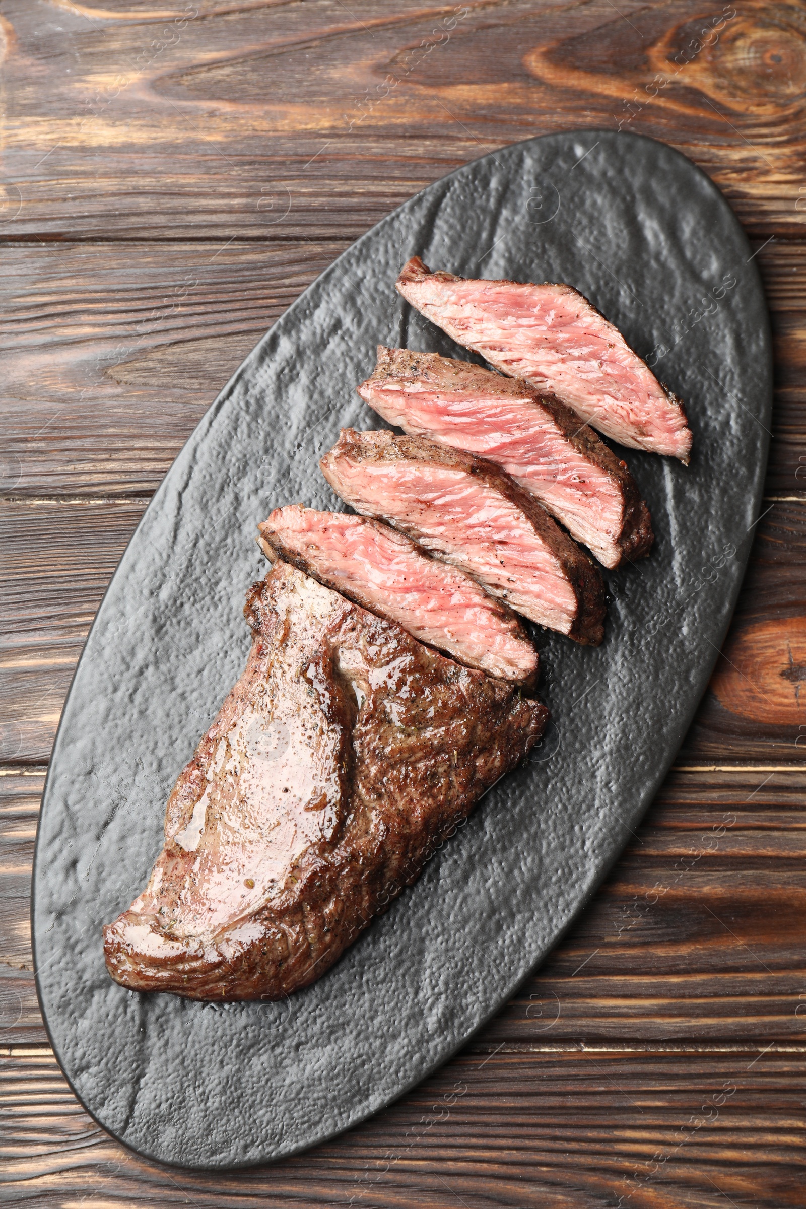 Photo of Pieces of delicious grilled beef meat on wooden table, top view