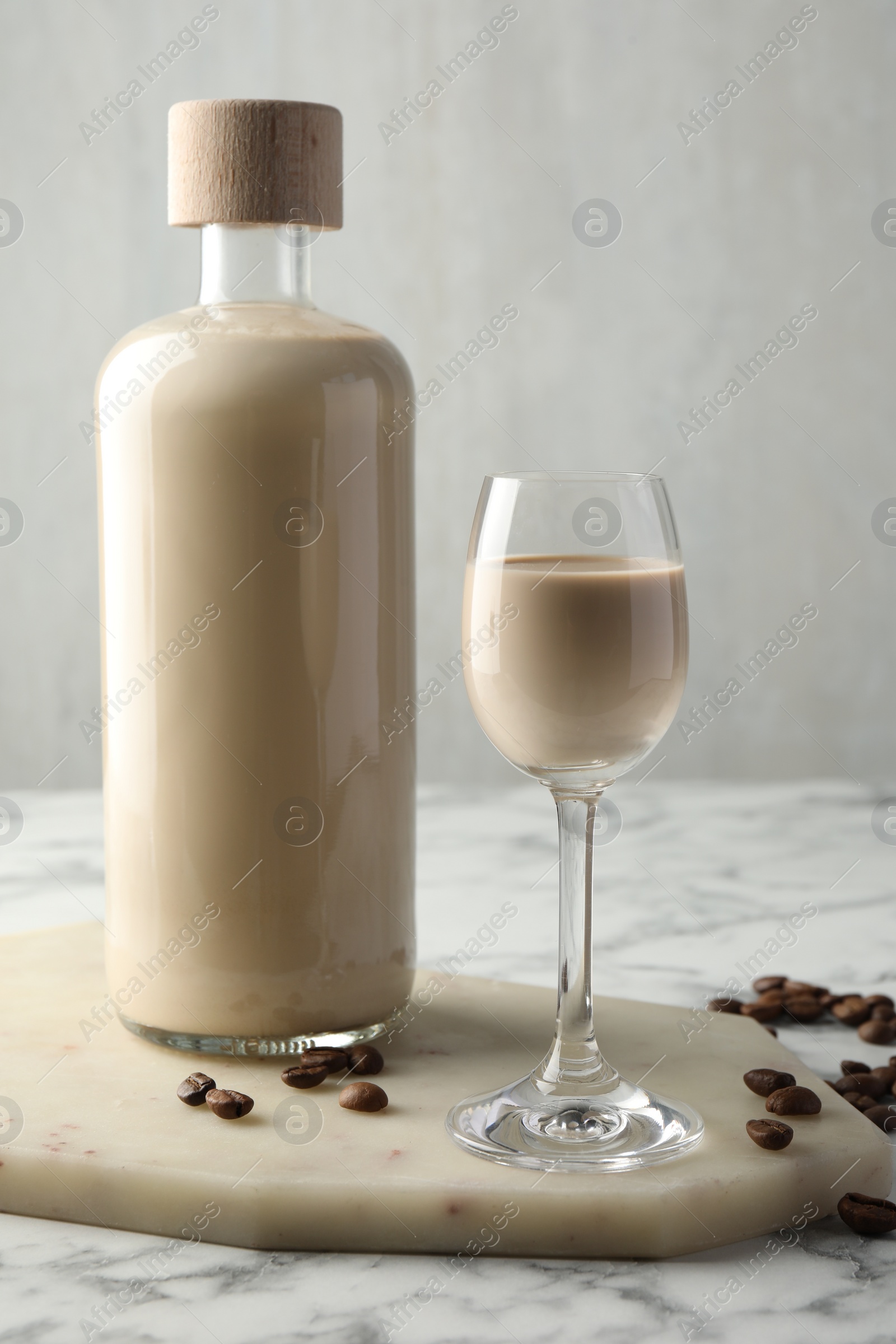 Photo of Coffee cream liqueur in glass, beans and bottle on white marble table