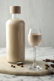 Coffee cream liqueur in glass, beans and bottle on white marble table