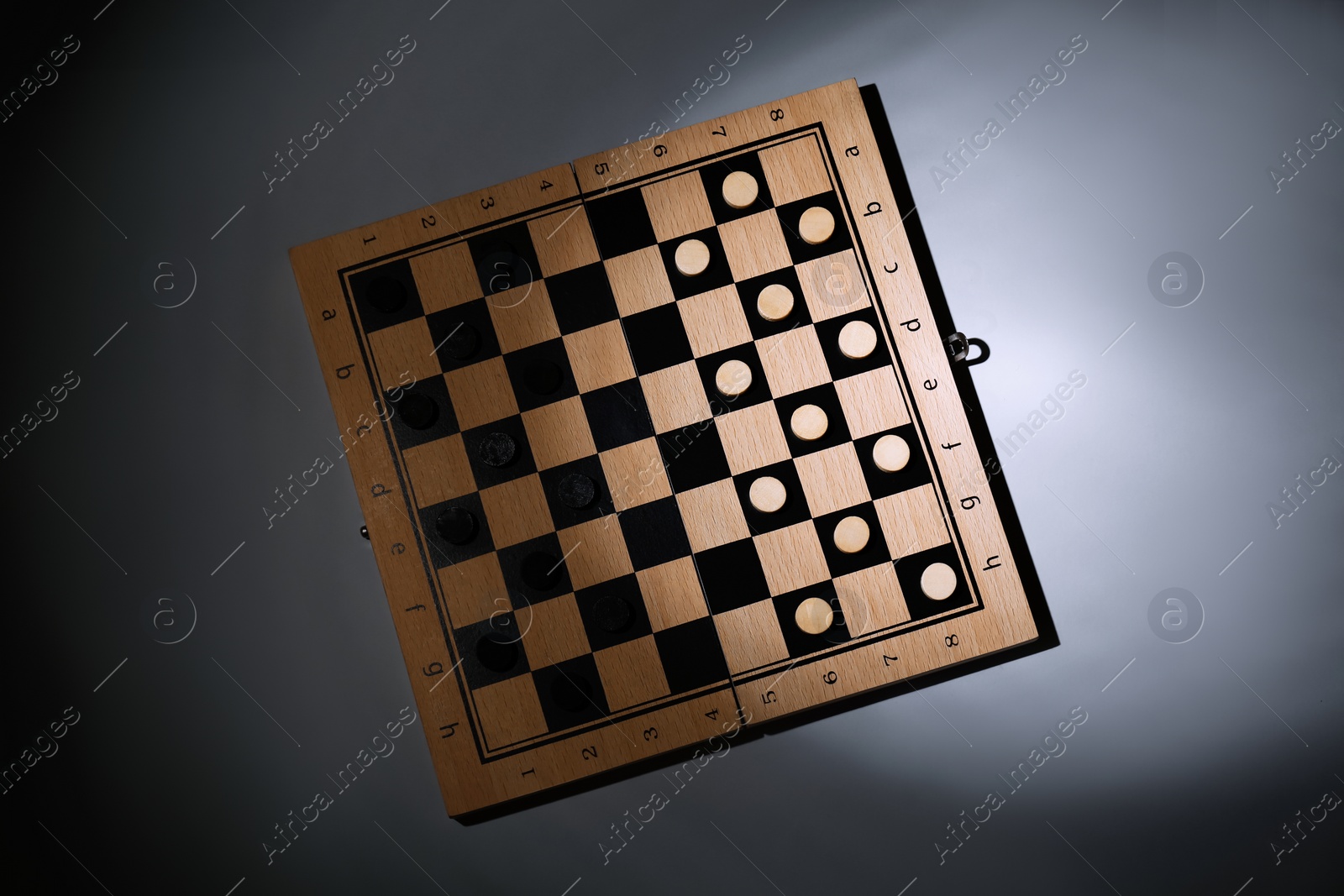 Photo of Wooden checkerboard with game pieces on grey background, top view