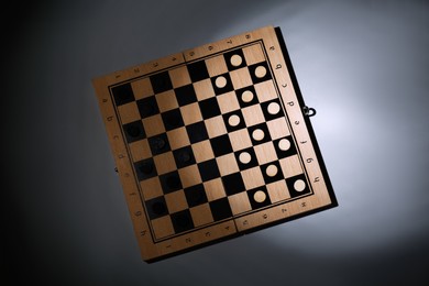 Photo of Wooden checkerboard with game pieces on grey background, top view