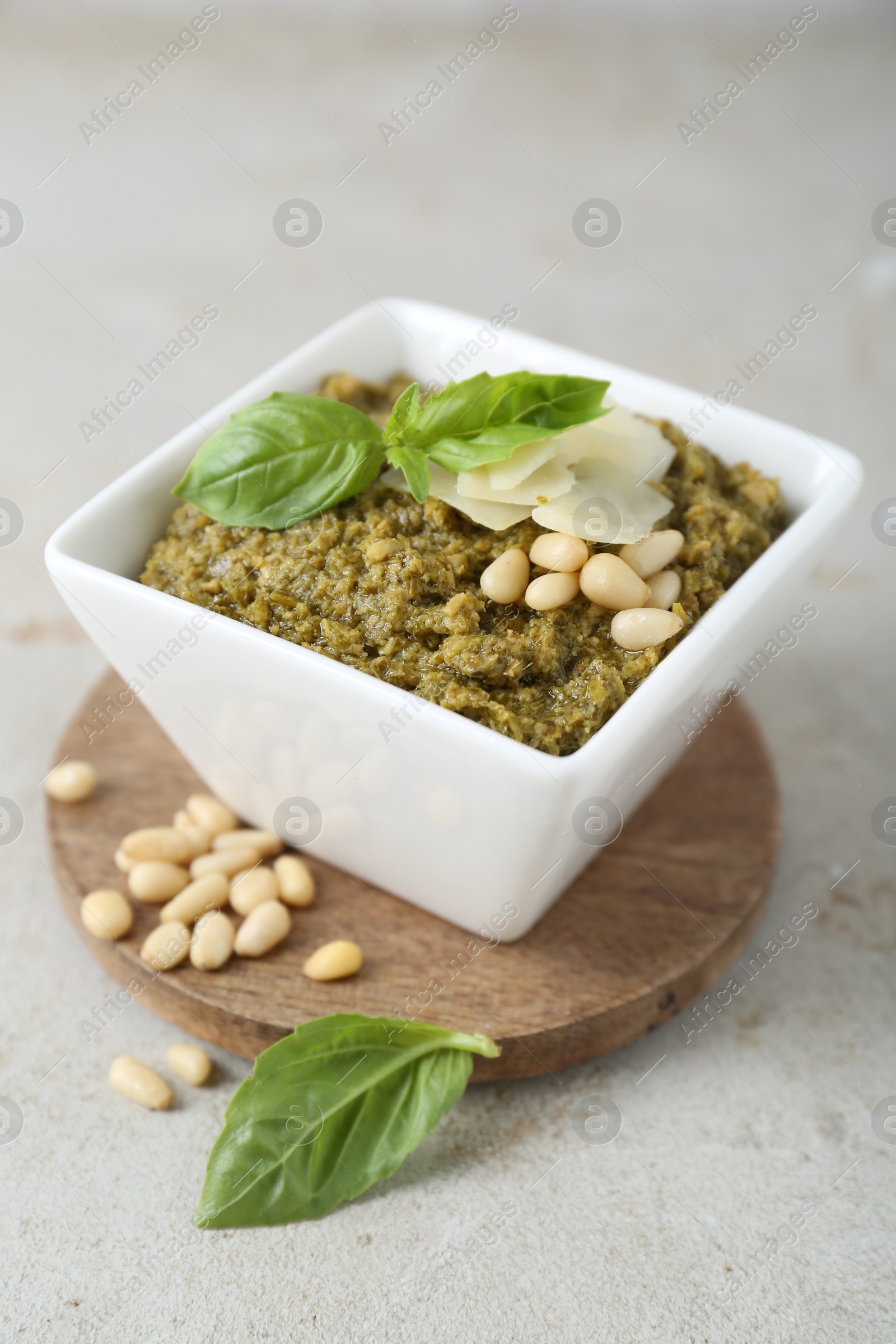 Photo of Bowl with delicious pesto sauce, cheese, pine nuts and basil leaves on light table, closeup