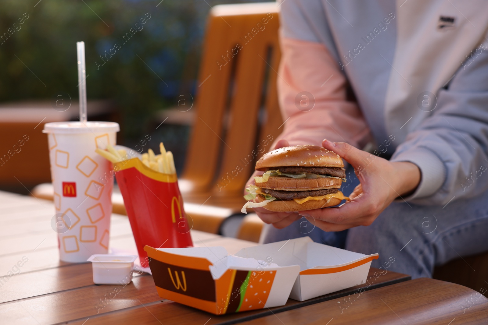 Photo of Lviv, Ukraine - September 26, 2023: Woman with McDonald's menu at wooden table outdoors, closeup