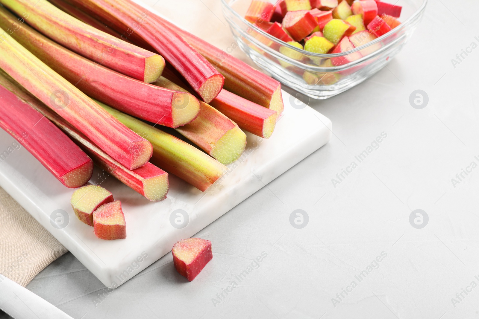 Photo of Whole and cut rhubarb stalks on white table, closeup. Space for text