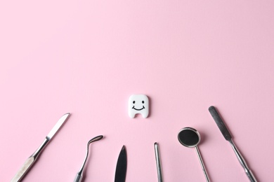 Professional dental tools and small plastic tooth on color background, flat lay