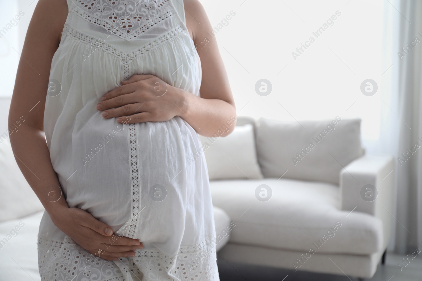 Photo of Pregnant young woman touching belly at home, closeup. Space for text